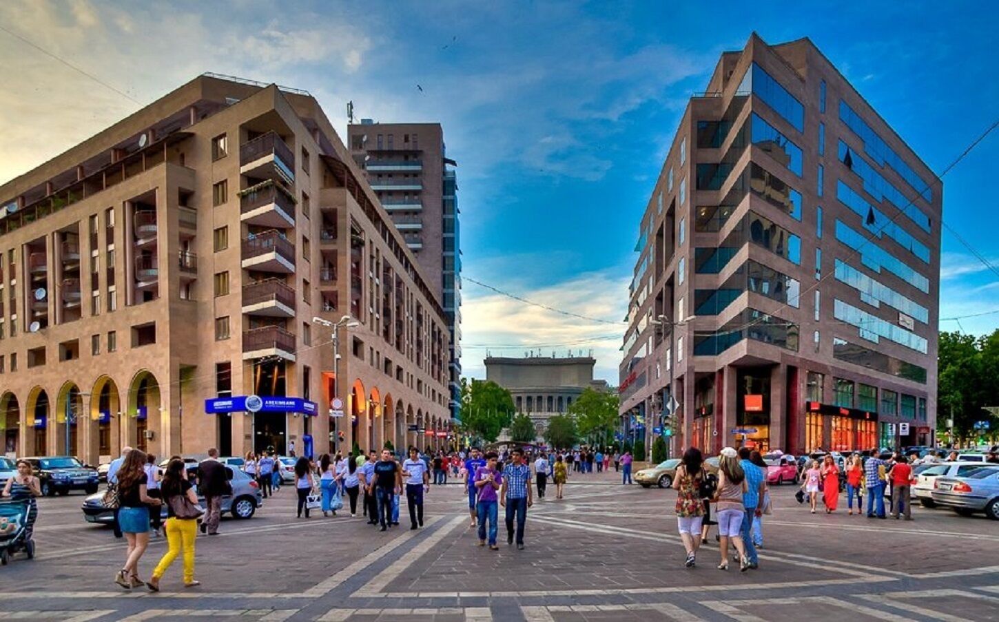 A busy urban street with modern buildings, pedestrians, and parked cars.