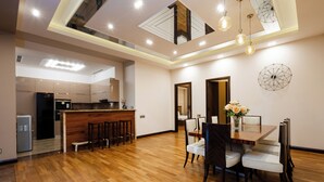 A spacious kitchen with a wooden countertop and bar stools, a dining area with a wooden table and chairs, and a modern ceiling design with recessed lighting.