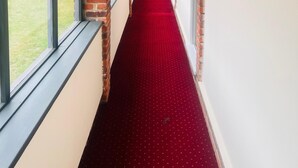 A corridor with brick walls, large windows, and a red carpet. - Rivenhall End Hotel (Witham)