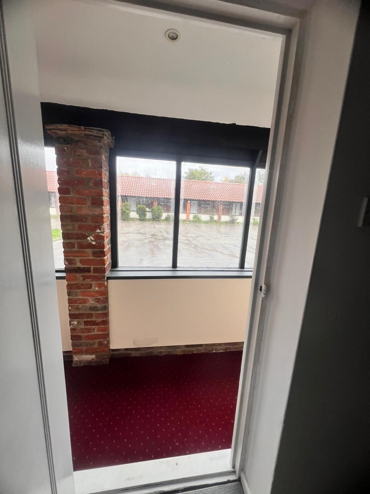 A room with a large window, a brick pillar, and a red carpet.