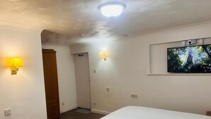 A hotel room with a bed, a TV mounted on the wall, and two wall-mounted lamps. - Rivenhall End Hotel (Witham)