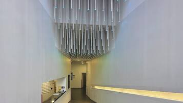 A modern, minimalist hallway with a unique ceiling light fixture and a reception desk on the left.