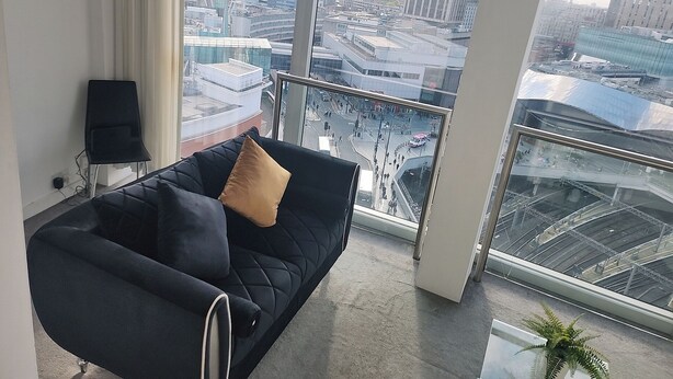 A modern living room with a black sofa and a view of a cityscape through large windows. - Cityscape Apartment in Rotunda Bham (Birmingham)