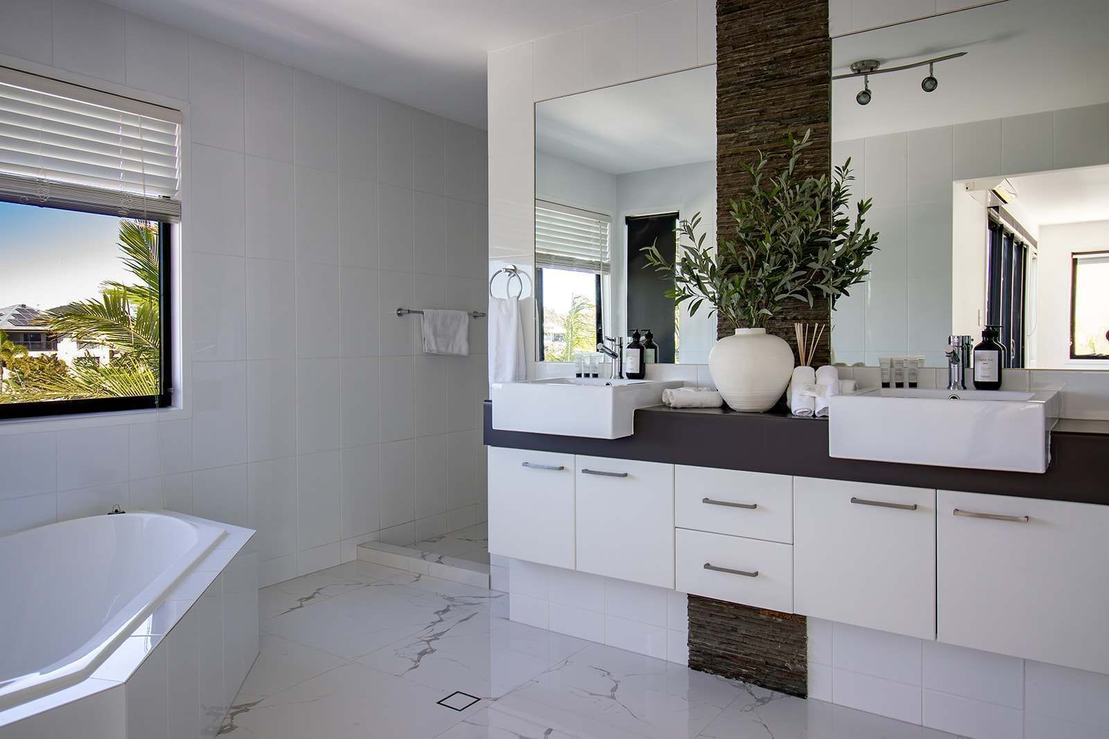 Ein modernes Badezimmer mit einer großen Badewanne, einem Waschtisch mit Spiegel und einer Topfpflanze.