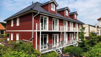 Un bâtiment rouge à deux étages, doté de balcons, d’un espace extérieur couvert aménagé en coin salon et d’un chemin en briques menant à l’entrée.