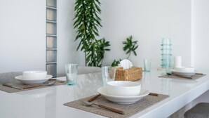 Une table à manger dressée avec de l’assiette, des bols et des couverts blancs, accompagnée de verres et d’un panier en osier.