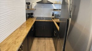Een compacte keuken met een houten aanrechtblad, roestvrijstalen apparatuur en een witte betegelde spatwand.
