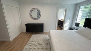 Een slaapkamer met een bed, een kast, een spiegel en een raam met jaloezieën.