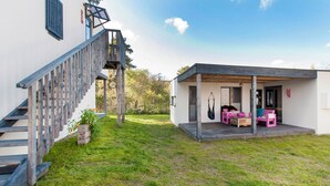 Een modern huis met een houten trap, een overdekte veranda met zitplaatsen en een verzorgd gazon.