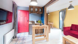 Een klein leefruimte met een kitchenette, een rode deur, een houten tafel en een rode bank.