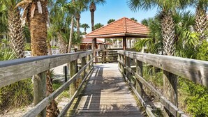 A wooden boardwalk leading to a building with a red-tiled roof, surrounded by palm trees.