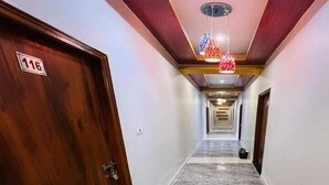 Um corredor com piso de mármore, portas de madeira e teto com luminárias pendentes.