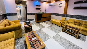 Um hall de entrada com balcão de recepção, sofás, mesa de centro com um jogo de tabuleiro e um relógio na parede.