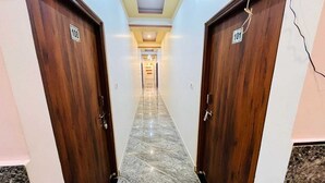 Um corredor com duas portas de madeira, cada uma com um número. O chão é de mármore e as paredes são brancas.