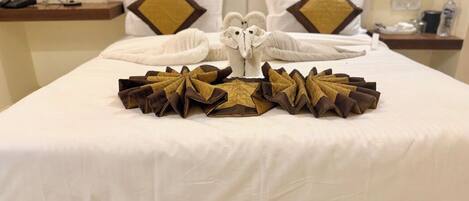 A neatly made bed with a decorative towel arrangement featuring a central towel shaped like an owl.