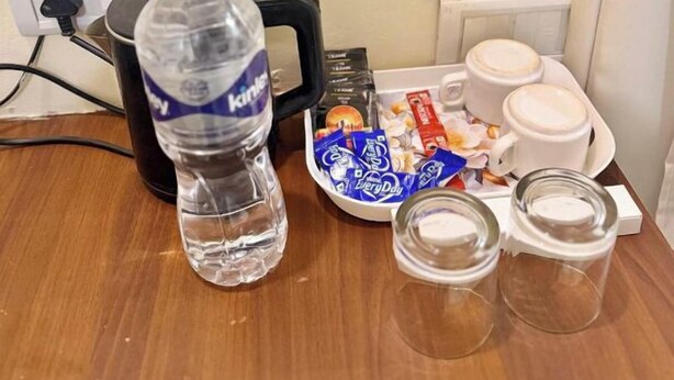 A hotel room with a water bottle, a tray with snacks, a coffee maker, and glasses.
