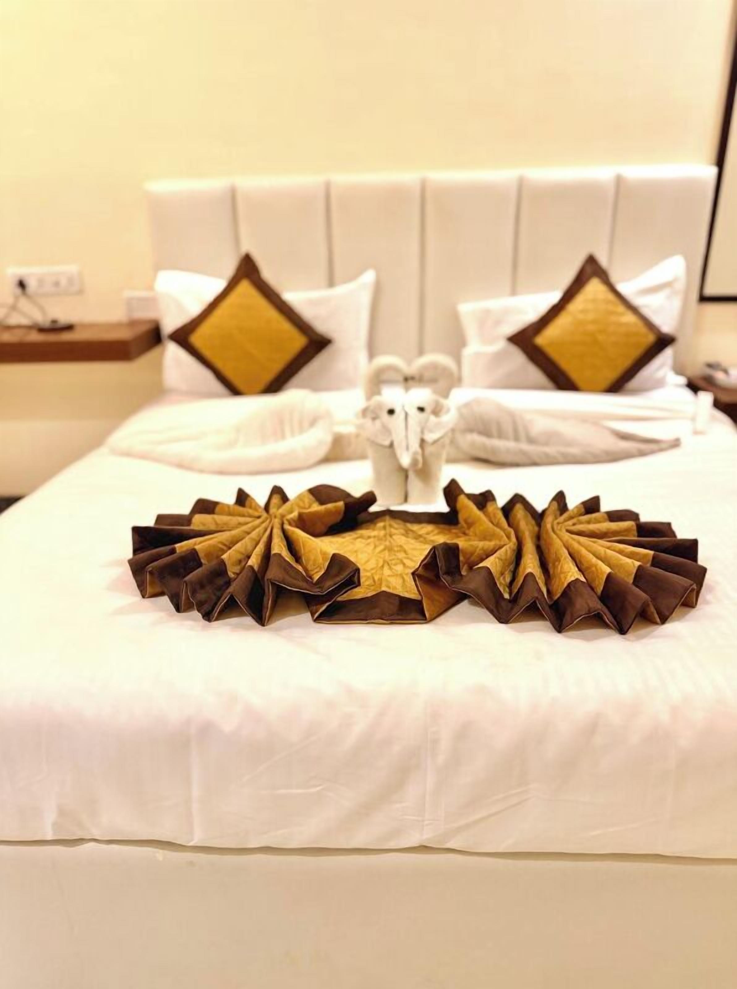Cama bem arrumada com almofadas brancas e douradas, um par de chinelos brancos e um tecido marrom e dourado decorativo na cama.