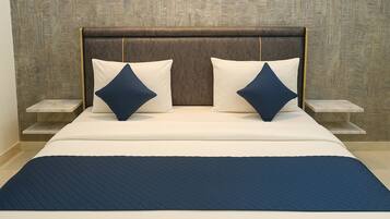 A bed with a quilted blue cover, two white pillows, and a dark brown headboard. There are two bedside tables with white marble tops.