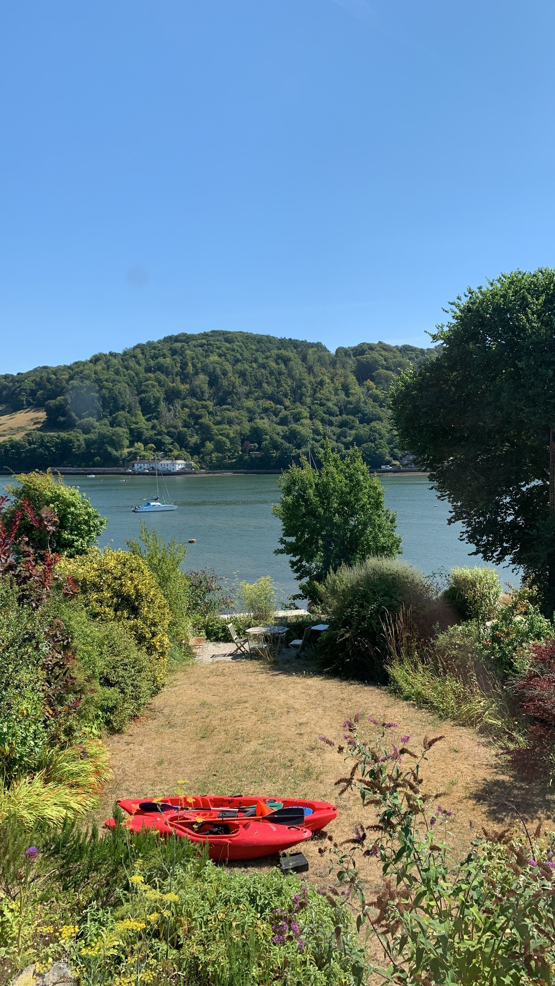 A lakeside view with a red kayak, a grassy area, and a house in the background.