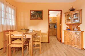 Un coin repas avec une table et des chaises en bois, une cuisine en arrière-plan et un meuble avec des portes en verre.