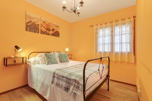 Une chambre à coucher comprenant un lit, des tables de chevet, un lustre, une fenêtre avec des rideaux et des œuvres d’art murales.
