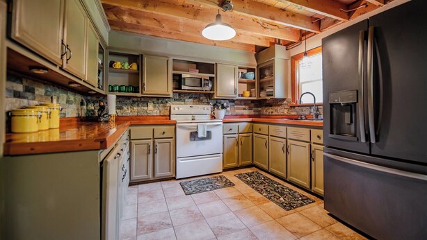 A kitchen with wooden ceiling beams, a stove, cabinets, a refrigerator, and a stone backsplash. - Cornerstone Escape - Robin Vacation Rentals (Benton)