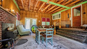 A rustic cabin interior with a brick fireplace, wooden walls, a dining table with chairs, and a staircase leading to a porch. - Cornerstone Escape - Robin Vacation Rentals (Benton)