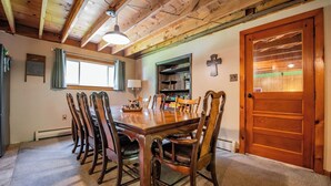 A dining area with a wooden table and chairs, a window with curtains, a cross on the wall, and a door with a window. - Cornerstone Escape - Robin Vacation Rentals (Benton)