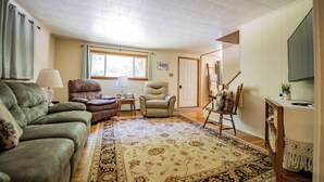 A living room with a sofa, two armchairs, a rug, a painting on easel, and a television. - Cornerstone Escape - Robin Vacation Rentals (Benton)
