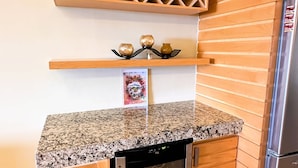 A kitchen with a granite countertop, a built-in dishwasher, a stainless steel refrigerator, wooden wall paneling, and a decorative shelf with three vases. - Anana El Dorado 305 Condo With Pool Lake Views (Chapala)