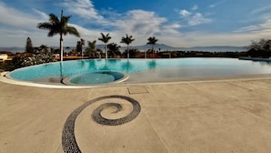 A large, empty swimming pool with a spiral design in the center, surrounded by palm trees and a clear sky. - Anana El Dorado 305 Condo With Pool Lake Views (Chapala)