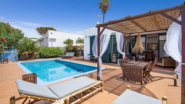 Uma área de piscina com espreguiçadeiras, uma mesa e um espaço de estar coberto.