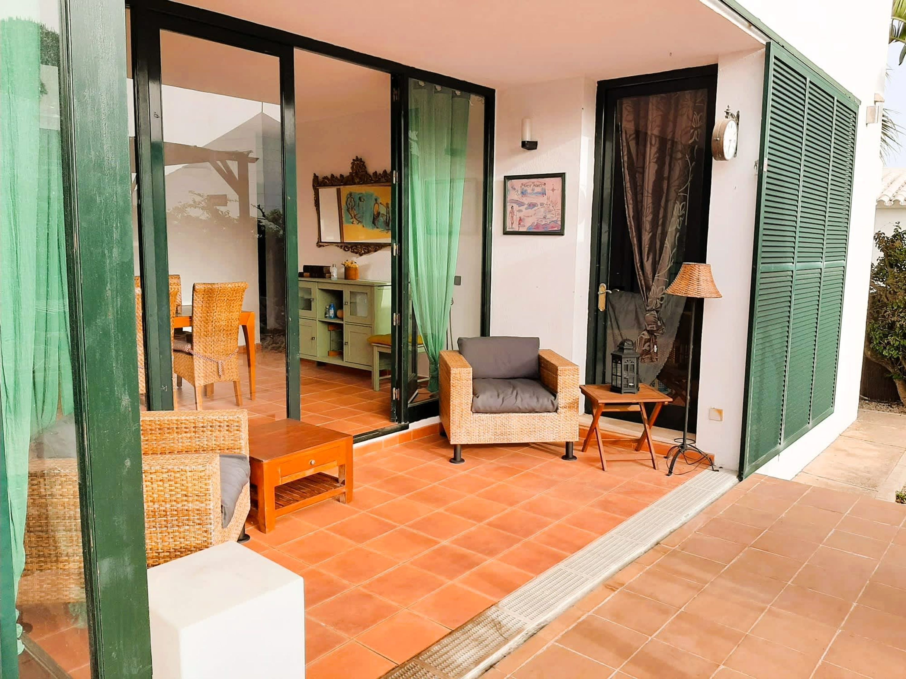 A room with a tiled floor, a sofa, a chair, a small table, and a cabinet.