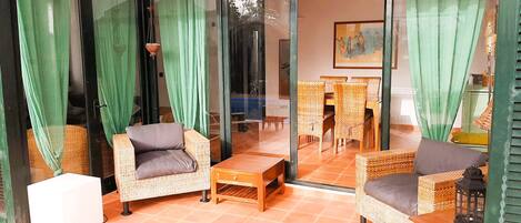 A room with a glass door, wicker furniture, and a tiled floor.