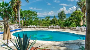 A swimming pool with a curved edge, surrounded by stone tiles and a variety of plants. - Anana Rancho San Rafael Villa With Pool Views (Chapala)