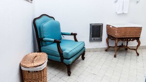 A corner room with a blue upholstered chair, a wicker basket, a metal vent, and a white tiled floor. - Anana Rancho San Rafael Villa With Pool Views (Chapala)