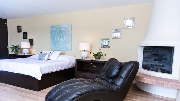 A modern bedroom with a bed, a chaise lounge, a fireplace, and wall art. - Anana Rancho San Rafael Villa With Pool Views (Chapala)