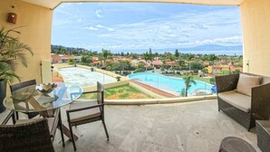 A balcony with a glass table and chairs, overlooking a swimming pool and a residential area. - Anana El Dorado 203 Condo With Lake Views Pool (Chapala)