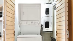 A compact laundry room with a front-loading washer and dryer, a water heater, and storage shelves. - Anana El Dorado 203 Condo With Lake Views Pool (Chapala)