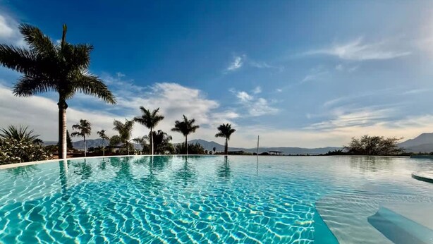 A clear blue pool with palm trees and mountains in the background. - Anana El Dorado 203 Condo With Lake Views Pool (Chapala)