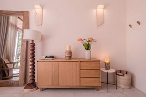 Un mueble de madera con una lámpara blanca, un jarrón con flores y una mesita con una vela.