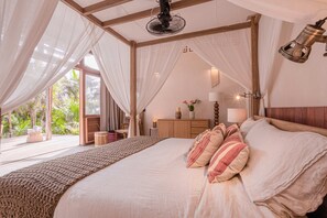 Ein Schlafzimmer mit einem großen Bett, einem hölzernen Kopfteil, einem Nachttisch, einer Lampe und Blick ins Freie.