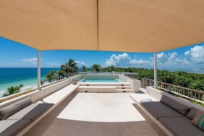 Ein überdachter Außenbereich mit Pool, Sitzgelegenheiten und Blick auf den Ozean.