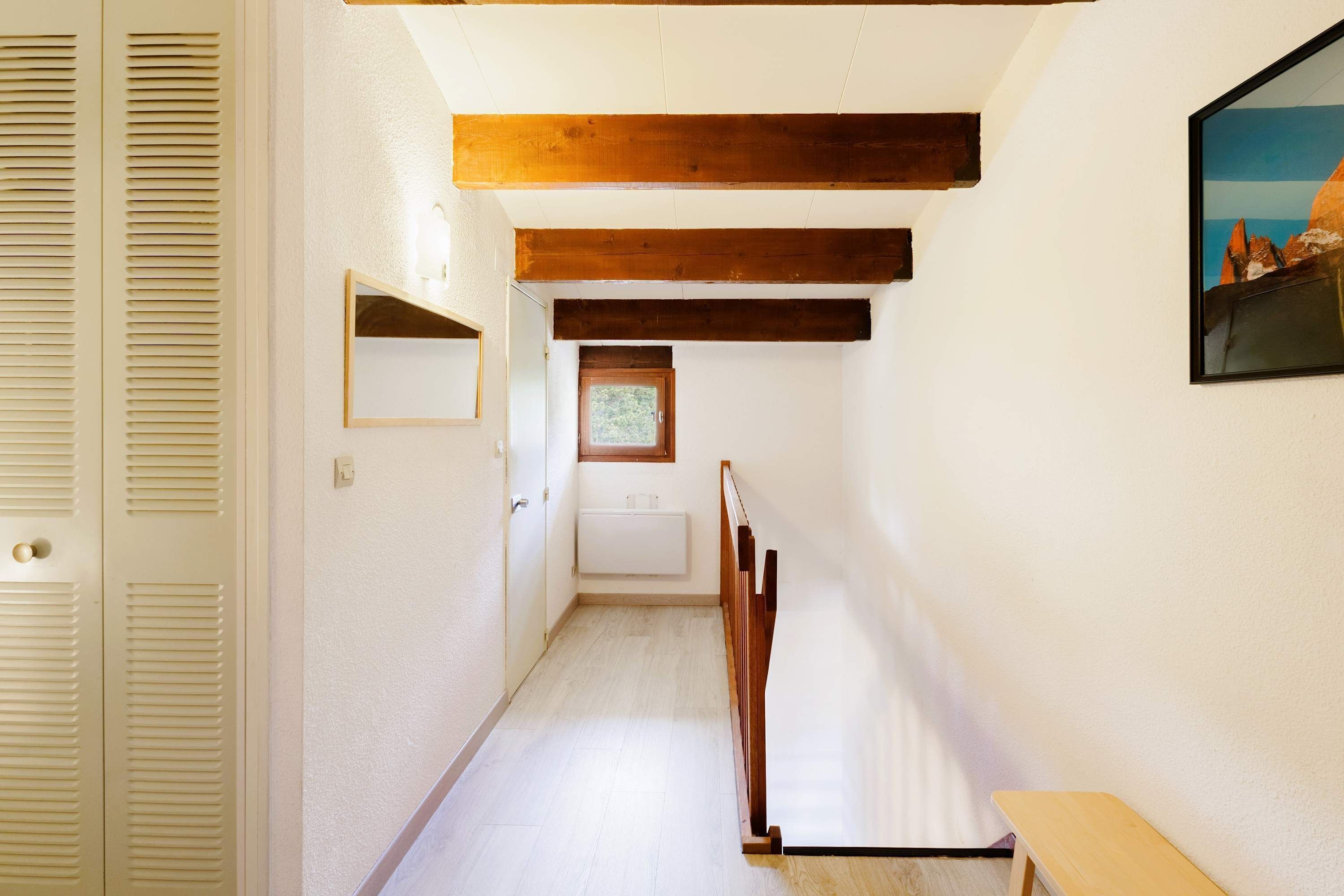 A narrow hallway with wooden beams, a white radiator, and a framed picture on the wall.