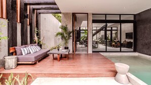 A modern interior with a wooden floor, a sofa, a table, and a small pool area. - Anana Casa Karmond Luxury Villa With Pool (Tulum)