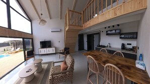 Amplia sala de estar con una mesa de comedor de madera, asientos cómodos, un televisor y vista a una piscina.