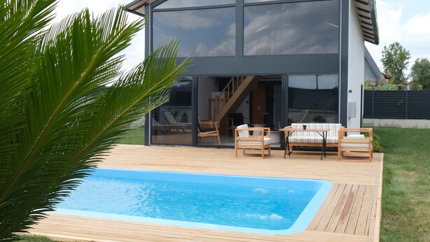 Una casa moderna con piscina, terraza de madera y zona de estar exterior.
