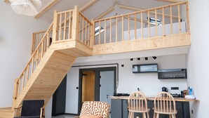 Un apartamento moderno estilo loft con una escalera de madera, un comedor con dos sillas y una cocina con un televisor sobre la encimera.