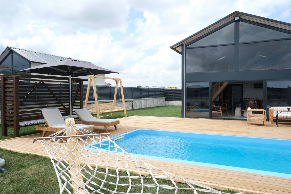 Une maison moderne dotée d’une piscine, d’une terrasse en bois et d’un espace salon extérieur.