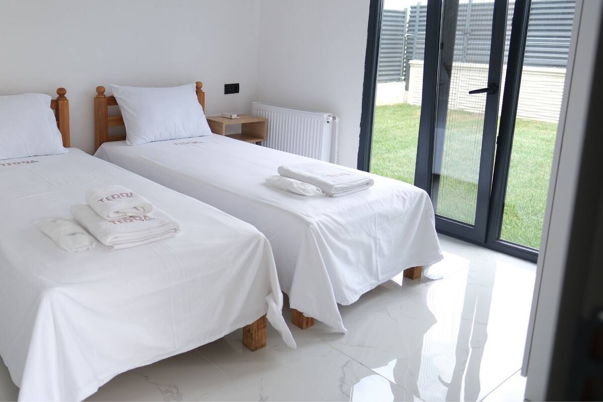 Une chambre d’hôtel avec deux lits, chacun doté d’une tête de lit en bois, de linge de lit blanc et d’une serviette portant la marque « Terra ».